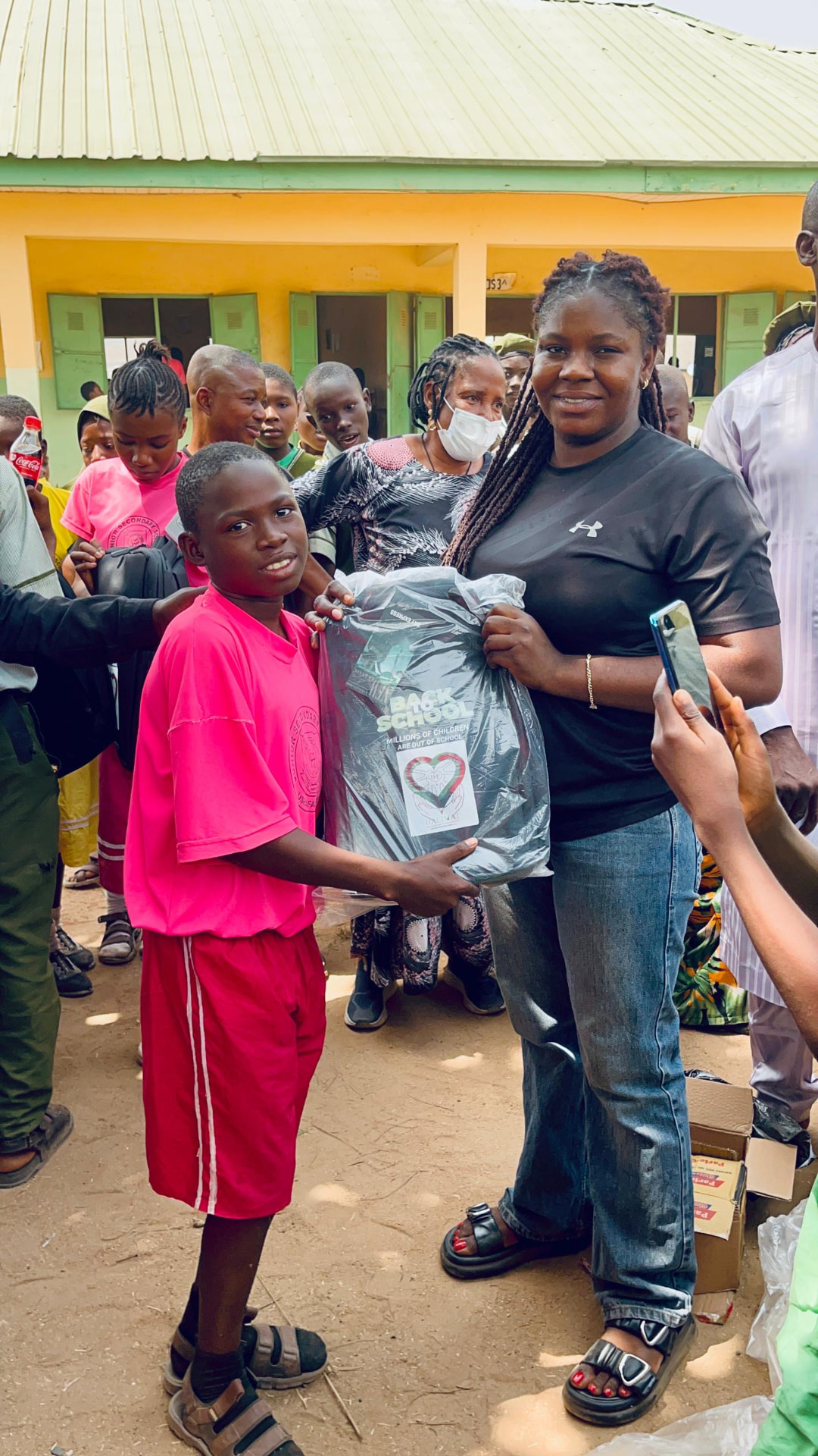 Foundation volunteer presenting a Back to School pack to a pupil in the school courtyard